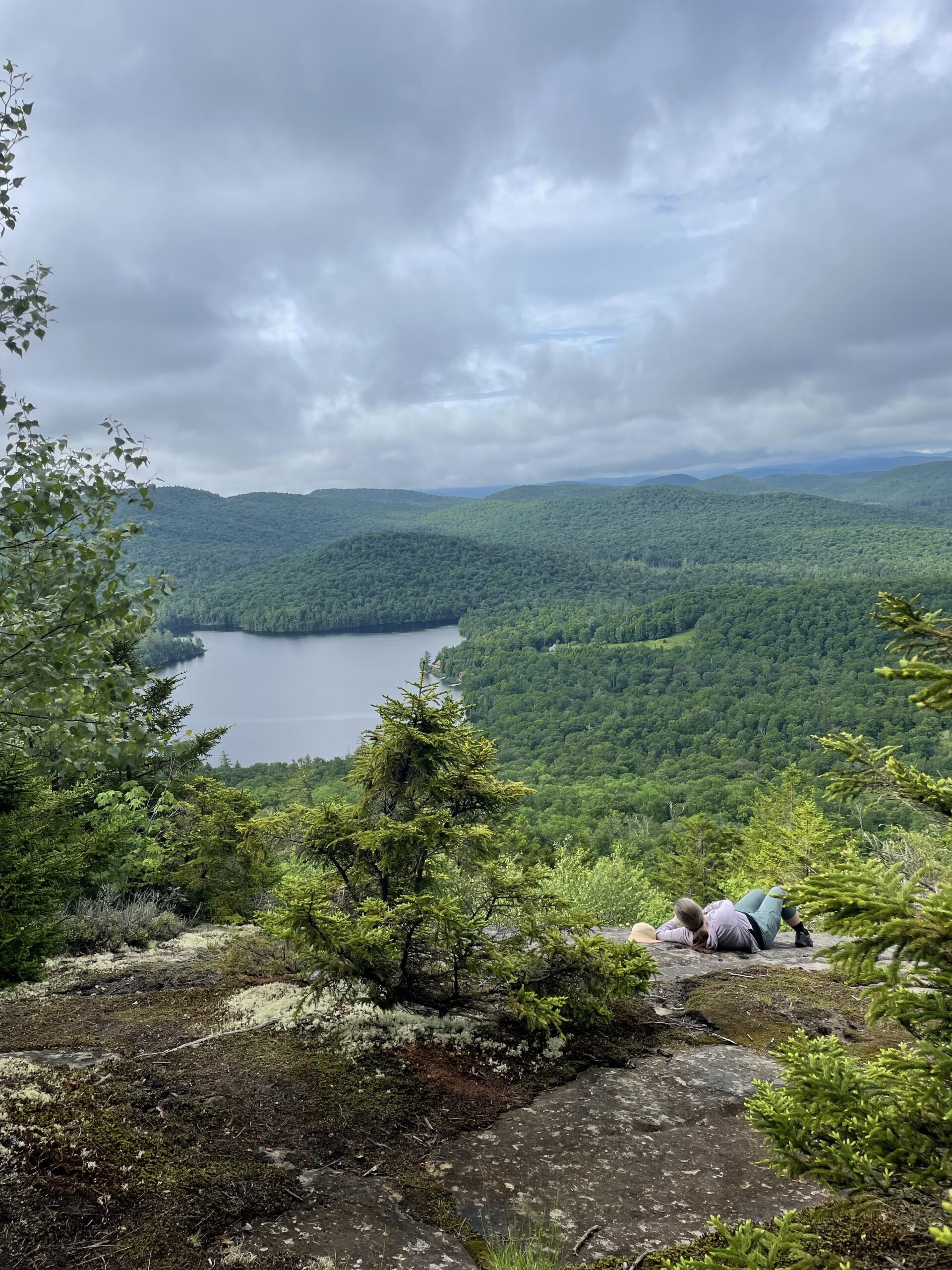 A person laying near a ledge outside looking out at mountains in the distance.